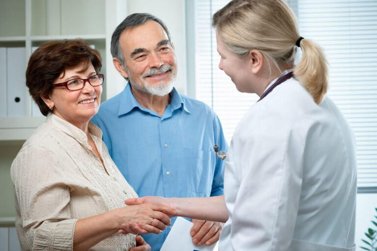 A female doctor greets a female patient as a man stands next to her.