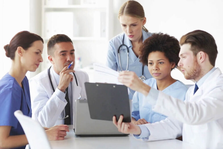 A group of doctors has a discussion while viewing a clipboard.